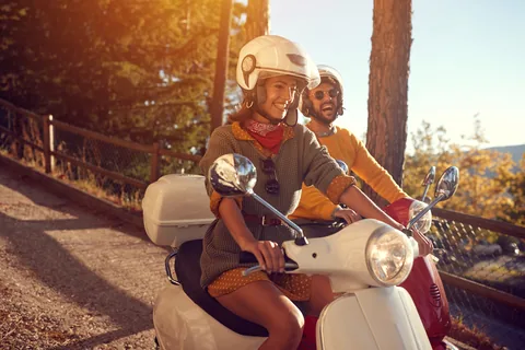 Couple riding a scooter through sunlit countryside